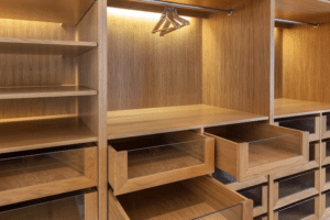 Interior de guarda-roupa planejado em madeira clara, com prateleiras apoiadas em suportes plásticos Oppeano, gavetas com frente de vidro e cabideiros iluminados.