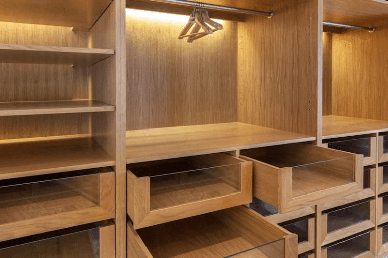 Interior de guarda-roupa planejado em madeira clara, com prateleiras apoiadas em suportes plásticos Oppeano, gavetas com frente de vidro e cabideiros iluminados.